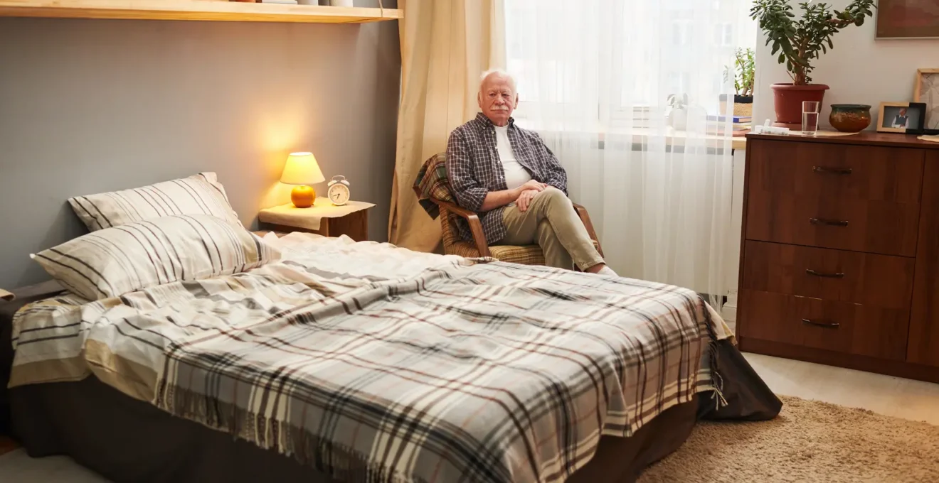 Chambre personnalisée d'EHPAD avec résidente âgée assise dans son fauteuil personnel entourée de photos de famille et objets familiers